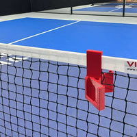 Indoor pickleball court with a red net clip on a blue court surface.